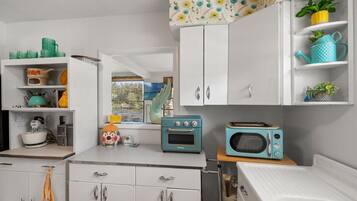 A kitchen with white cabinets, a microwave, a toaster, and a window with a view of greenery.