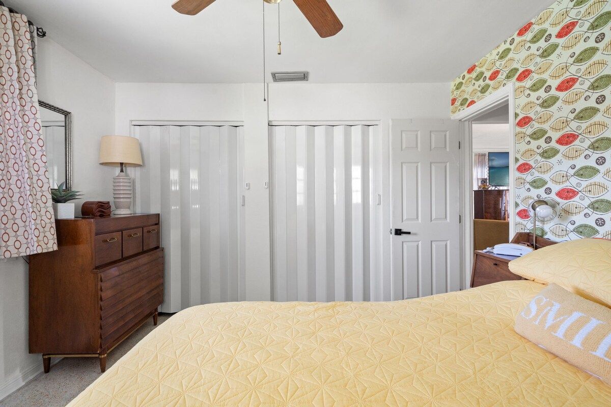 A bedroom with a bed, dresser, ceiling fan, and a door with a patterned curtain.