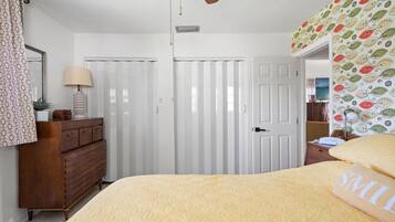 A bedroom with a bed, dresser, ceiling fan, and a door with a patterned curtain.