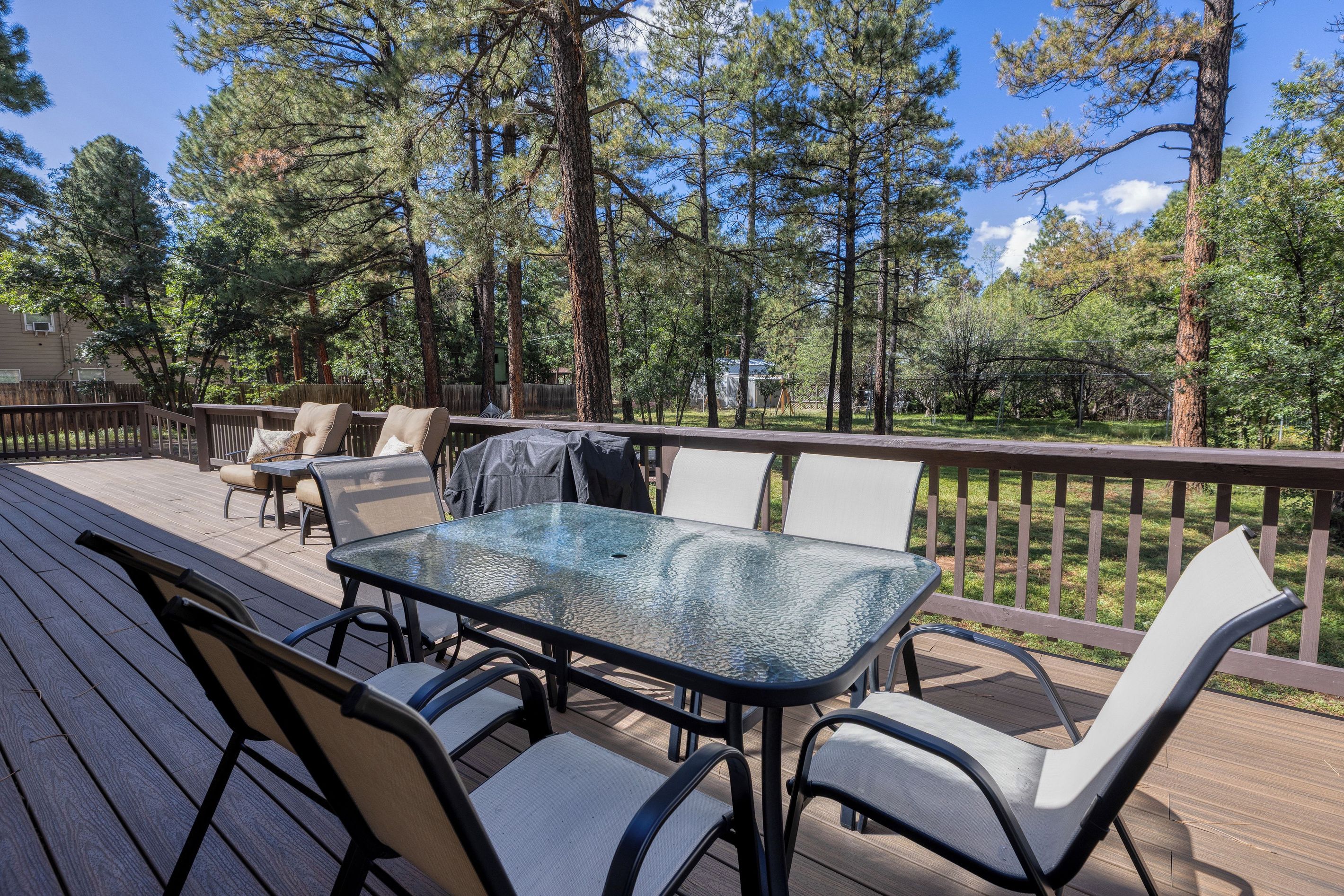 Une terrasse extérieure dotée d’une table et de chaises à plateau en verre, entourée d’une balustrade en bois et d’arbres.