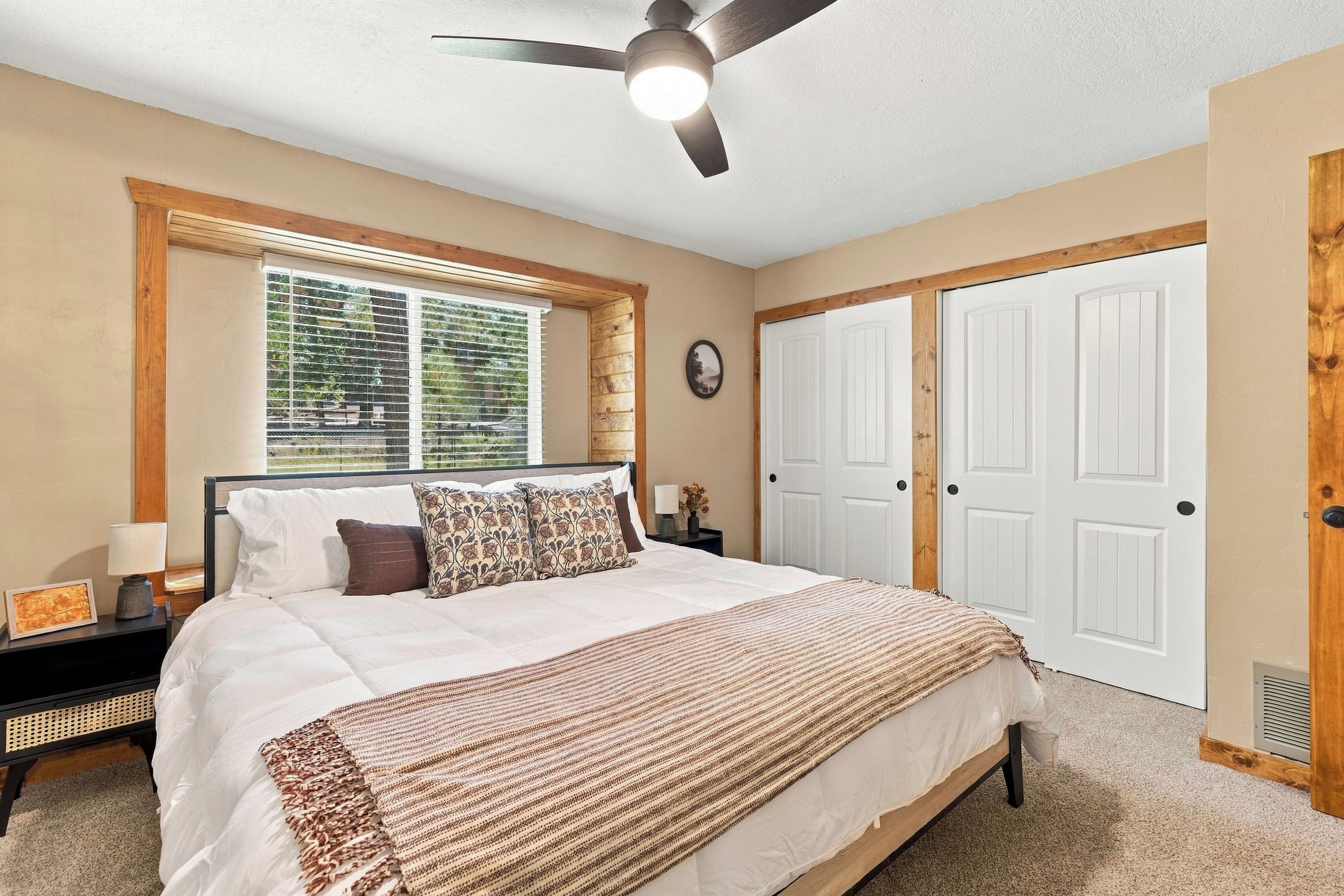 Une chambre à coucher avec un lit, un ventilateur de plafond, une fenêtre avec des stores et une porte.