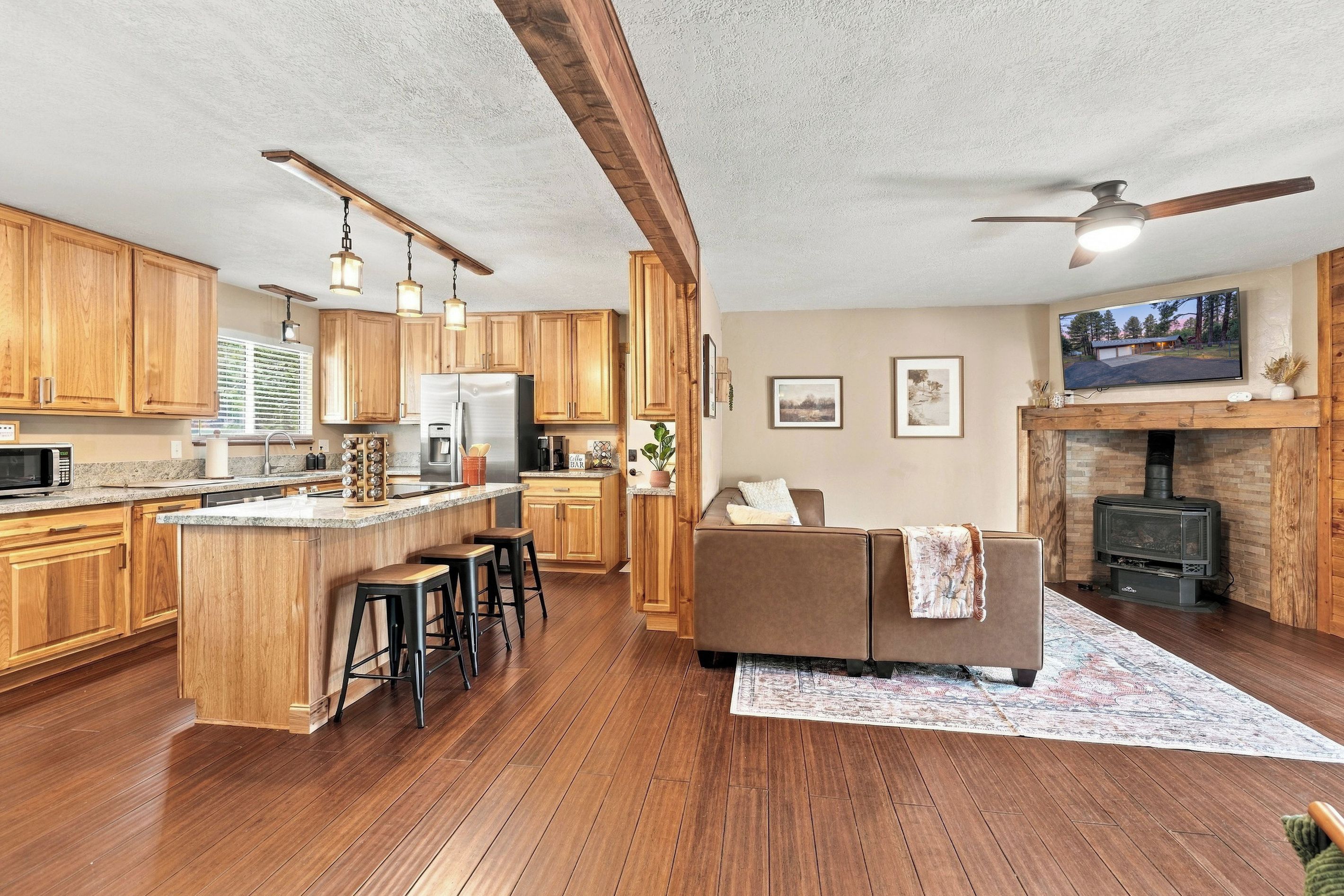 Eine geräumige Küche mit Holzschränken, einer zentralen Kochinsel mit Barhocker, einem eingebauten Herd und einem gemütlichen Wohnbereich mit Sofa und Kamin.
