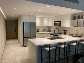 A modern kitchen with a central island, bar stools, and built-in appliances. - Playa Royale 2204 Beachfront apartment with a balcony and ocean view (Nuevo Nayarit)