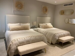 Quarto com duas camas, cada uma com cabeceira e peseira combinando, e um banco entre elas.