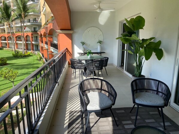 Uma varanda com mesa e cadeiras, um vaso de planta e vista para um edifício com varandas.