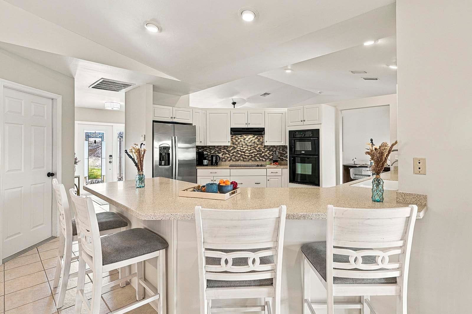 A modern kitchen with white cabinetry, a central island with bar stools, and built-in appliances.