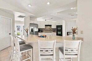 A modern kitchen with white cabinetry, a central island with bar stools, and built-in appliances. - The Dock House I Gulf Access I Southern Exposure Pool/Spa (Cape Coral)