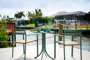 Ein Tisch mit Stühlen auf einem Steg, mit Blick auf Wasser und Gebäude im Hintergrund.
