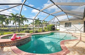 A covered swimming pool with a hot tub, surrounded by a patio area with a view of a residential neighborhood. - The Dock House I Gulf Access I Southern Exposure Pool/Spa (Cape Coral)