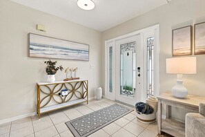 A modern entryway with a console table, a large painting, a decorative mirror, and a lamp. - The Dock House I Gulf Access I Southern Exposure Pool/Spa (Cape Coral)