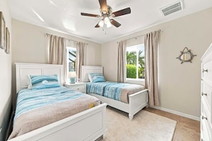 A bedroom with two single beds, a ceiling fan, a window with curtains, and a wall-mounted decorative item. - The Dock House I Gulf Access I Southern Exposure Pool/Spa (Cape Coral)