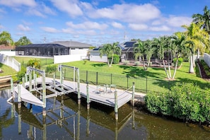 A waterfront property with a dock, a grassy lawn, and a clear sky. - The Dock House I Gulf Access I Southern Exposure Pool/Spa (Cape Coral)