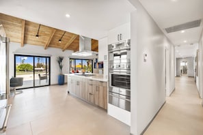 A modern kitchen with stainless steel appliances, a large island, and a view to the outdoors. - Stunning South Palm Desert Home with Private Pool, Spa & Shadow Mountain Golf Course Views (Palm Desert)