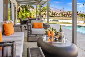 A covered outdoor seating area with wicker furniture and orange cushions, a pool, and a mountain view. - Stunning South Palm Desert Home with Private Pool, Spa & Shadow Mountain Golf Course Views (Palm Desert)