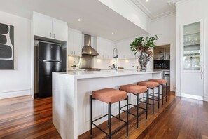 A modern kitchen with a central island, bar stools, a stainless steel refrigerator, and a decorative plant.