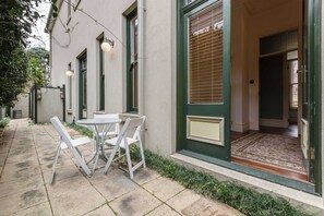 A building with a green door, a small outdoor seating area with a table and chairs, and a window with blinds. - VAQUAY The Marigold In Hawthorn (Hawthorn)