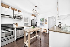 Eine moderne Küche mit weißen Schränken, Edelstahlgeräten, einem Holztisch und Blick ins Freie.