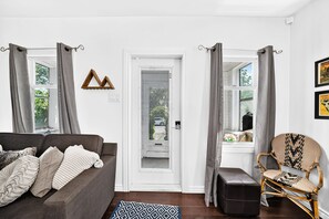 Ein Wohnzimmer mit einer Couch, einem Sessel, einer Tür und einem Fenster mit Vorhängen.