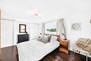 Ein Schlafzimmer mit einem Bett, einem Schminktisch, einem Sessel, einem Fenster mit Vorhängen und einer Wandlampe.