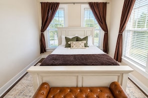 Un dormitorio con cama, cortinas, un banco y una ventana.