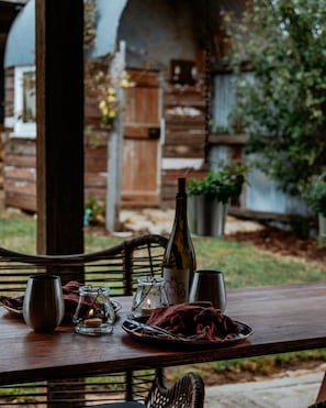 Mesa de comedor exterior con una botella, vasos y candelabros.