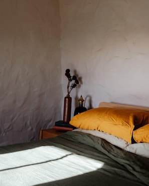 A bedroom with a bed, a nightstand, a vase with dried flowers, and a wall with a textured pattern.