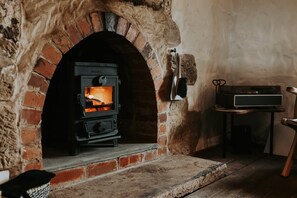 A wood-burning stove in a brick fireplace, a table with a speaker, and a chair.