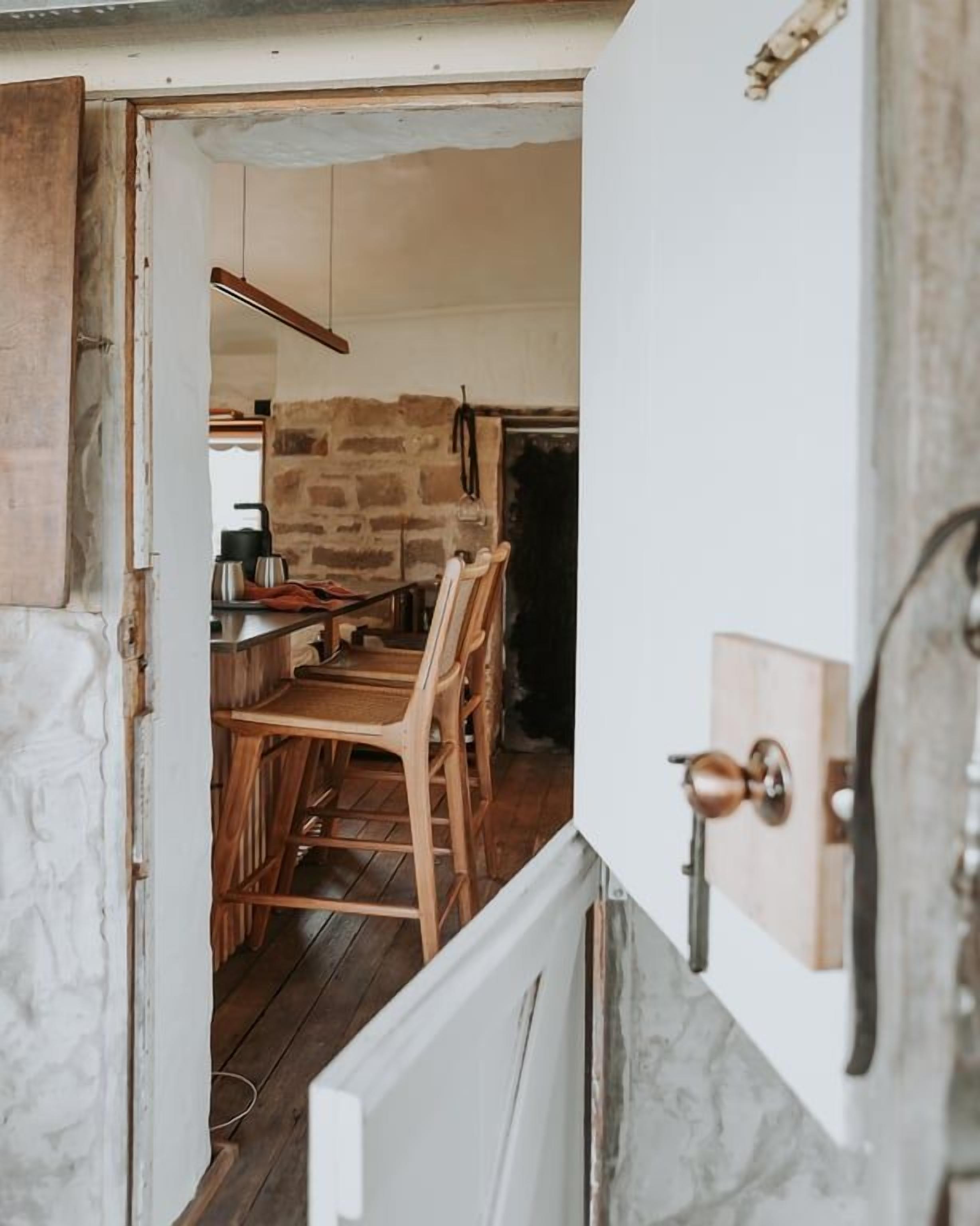 An open door leading to a dining area with wooden chairs and a table, a stone wall, and a hanging light fixture.