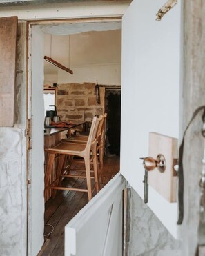 An open door leading to a dining area with wooden chairs and a table, a stone wall, and a hanging light fixture.