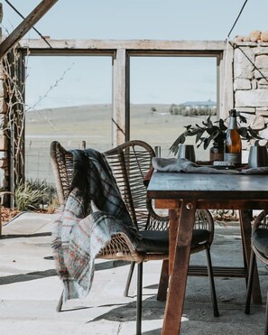 A rustic outdoor seating area with wicker chairs, a table, and a view of the countryside.