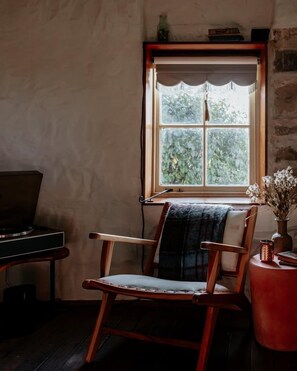 A room with a wooden rocking chair, a desk with a computer, and a window with a view of greenery.