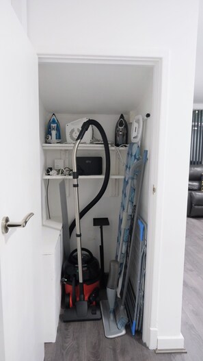 A compact storage area with a vacuum cleaner, ironing board, and a shelf with a box labeled 'sky'. - Charming Manchester House with 3 Bedrooms (Manchester)