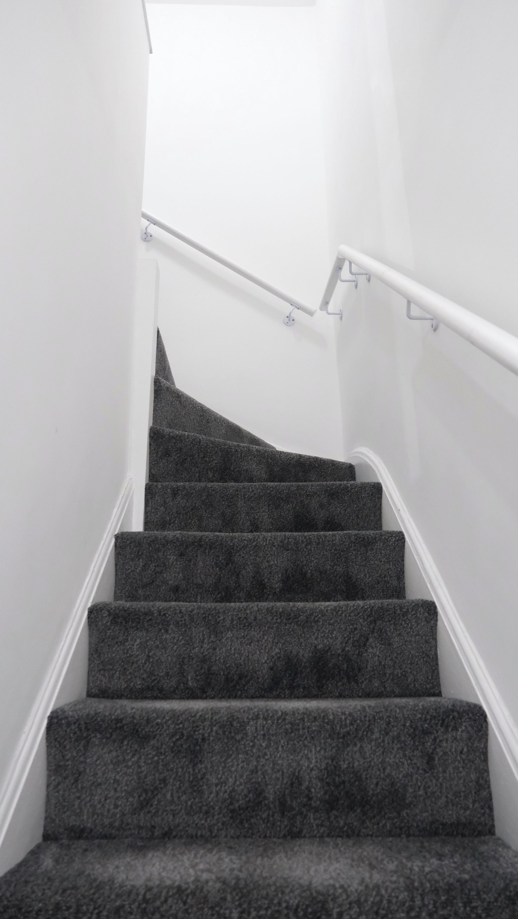 Eine Treppe mit Teppichstufen und weißen Handläufen.