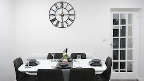 A dining area with a white table set for four, black chairs, a wall clock, and a door with frosted glass panels. - Charming Manchester House with 3 Bedrooms (Manchester)