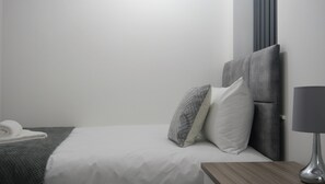A hotel room with a bed, a bedside table, a lamp, and a towel on the floor. - Charming Manchester House with 3 Bedrooms (Manchester)