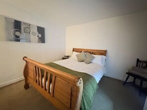 Quarto com cama de madeira, mesa de cabeceira, cadeira e um quadro na parede.