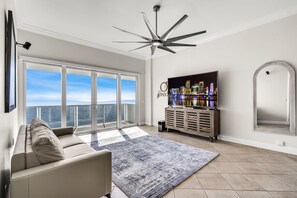 A spacious living room with a large window, a ceiling fan, a flat-screen TV, and a wooden cabinet. - Stunning Ocean View Penthouse in Hollywood, FL. (Hollywood)