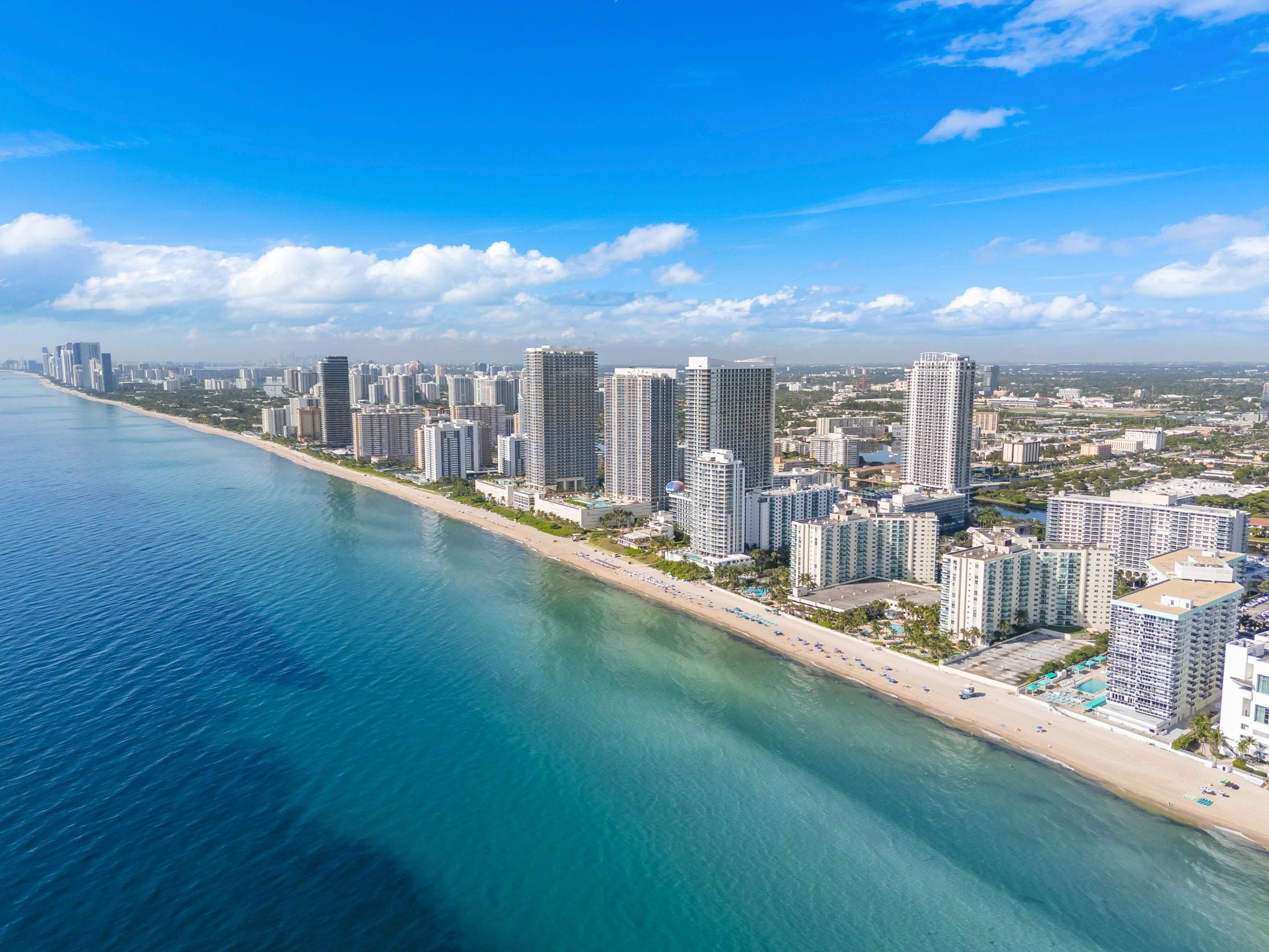 A coastal cityscape with high-rise buildings, a beach, and clear skies.