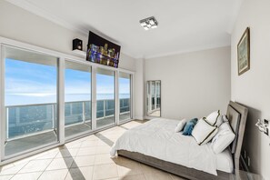 Een slaapkamer met een groot bed, stadszicht door raamwanden en een moderne plafondlamp.