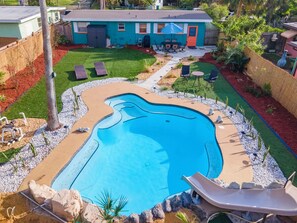 A swimming pool with a slide, surrounded by a landscaped garden with a patio area. - Beachside Retreat-Steps To Ocean-Private Heated Pool Oasis-Pet Friendly (Daytona Beach)