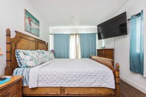 A neatly made bed with a quilted white cover, a wooden headboard, and a bedside table with a lamp. - Beachside Retreat-Steps To Ocean-Private Heated Pool Oasis-Pet Friendly (Daytona Beach)