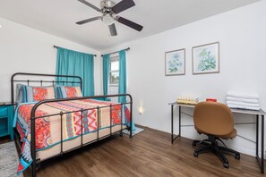 A bedroom with a bed, a desk, a chair, a ceiling fan, and two framed pictures on the wall. - Beachside Retreat-Steps To Ocean-Private Heated Pool Oasis-Pet Friendly (Daytona Beach)