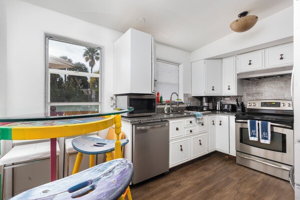 A modern kitchen with white cabinets, stainless steel appliances, and a wooden floor. - Beachside Retreat-Steps To Ocean-Private Heated Pool Oasis-Pet Friendly (Daytona Beach)