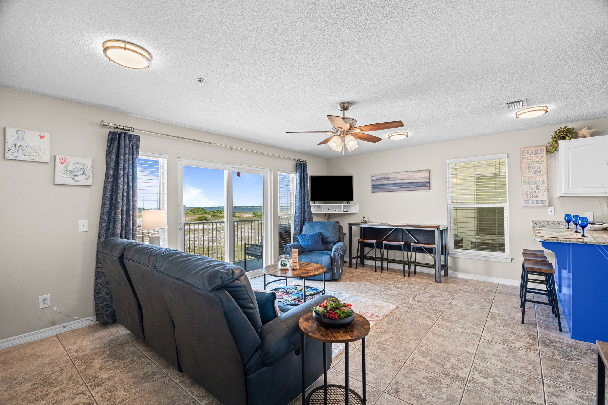 A modern living room with a sofa, a dining area with a table and chairs, a ceiling fan, and a view of the outdoors.