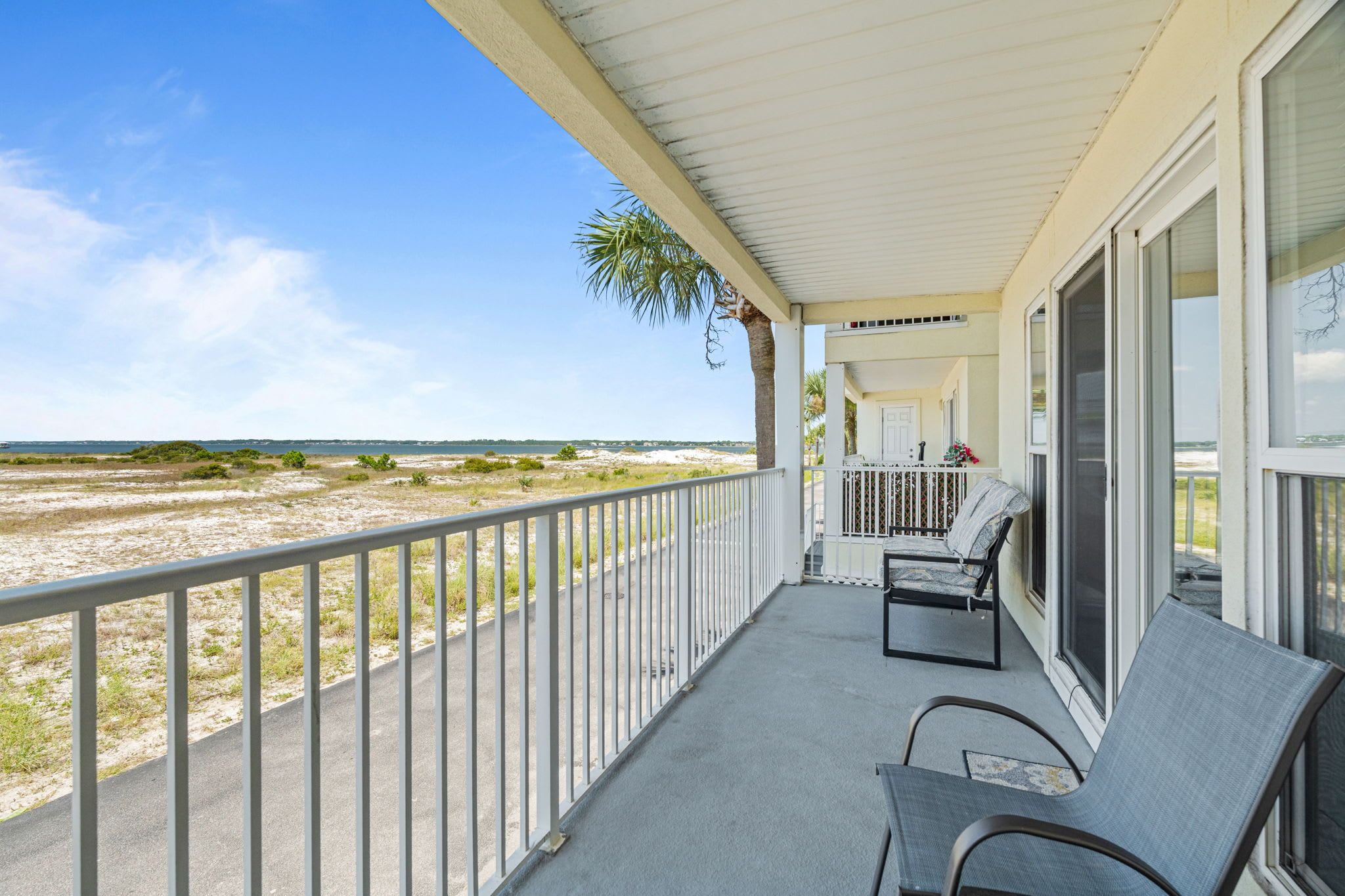 A covered balcony with a view of the beach, a chair, and a small table.