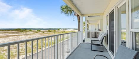 A covered balcony with a view of the beach, a chair, and a small table.