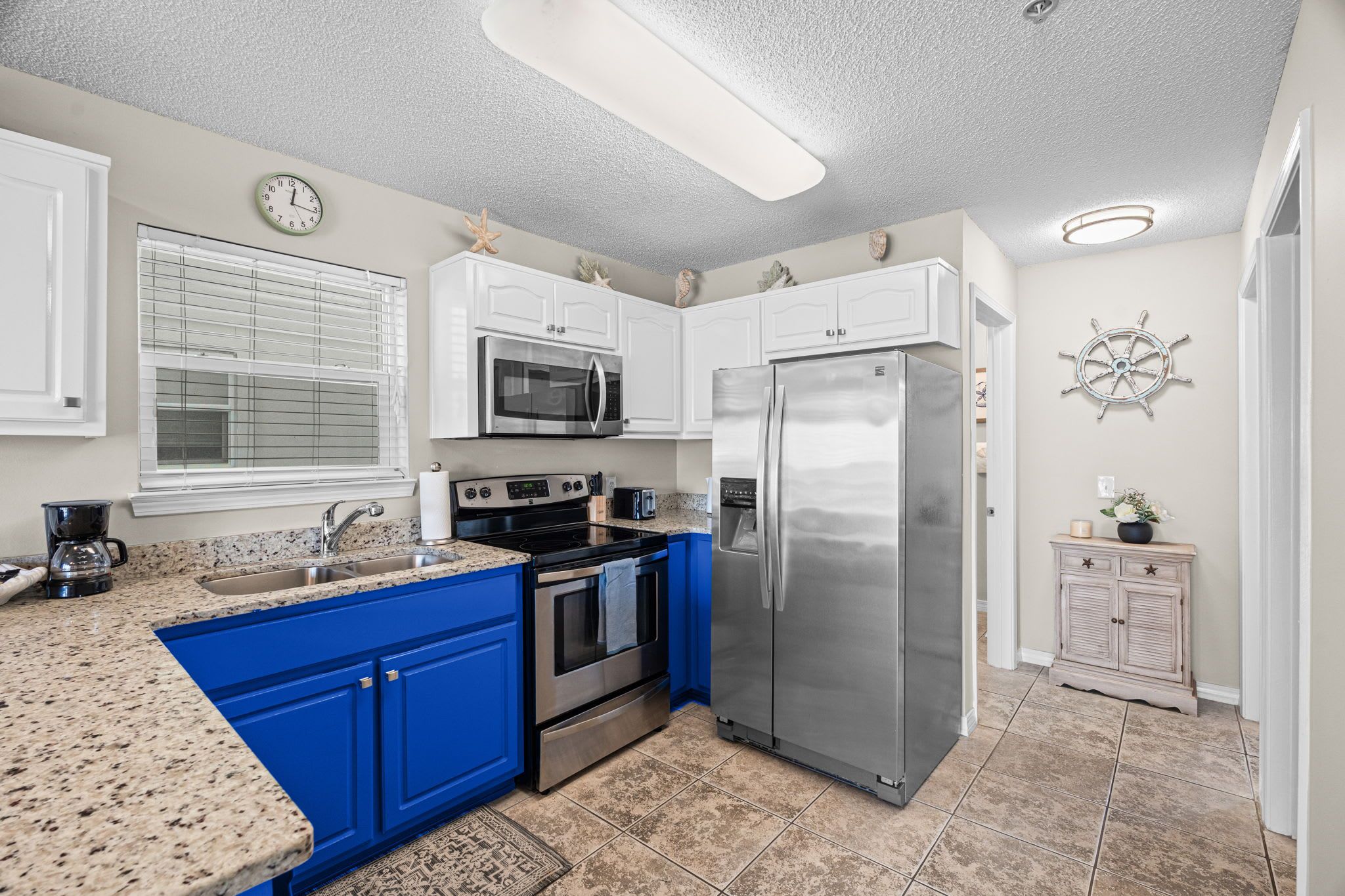 A kitchen with white cabinets, a blue island, stainless steel appliances, and a nautical-themed wall decoration.