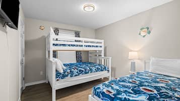 A bunk bed with a blue shark-themed bedspread, a bedside table with a lamp, and a white door.