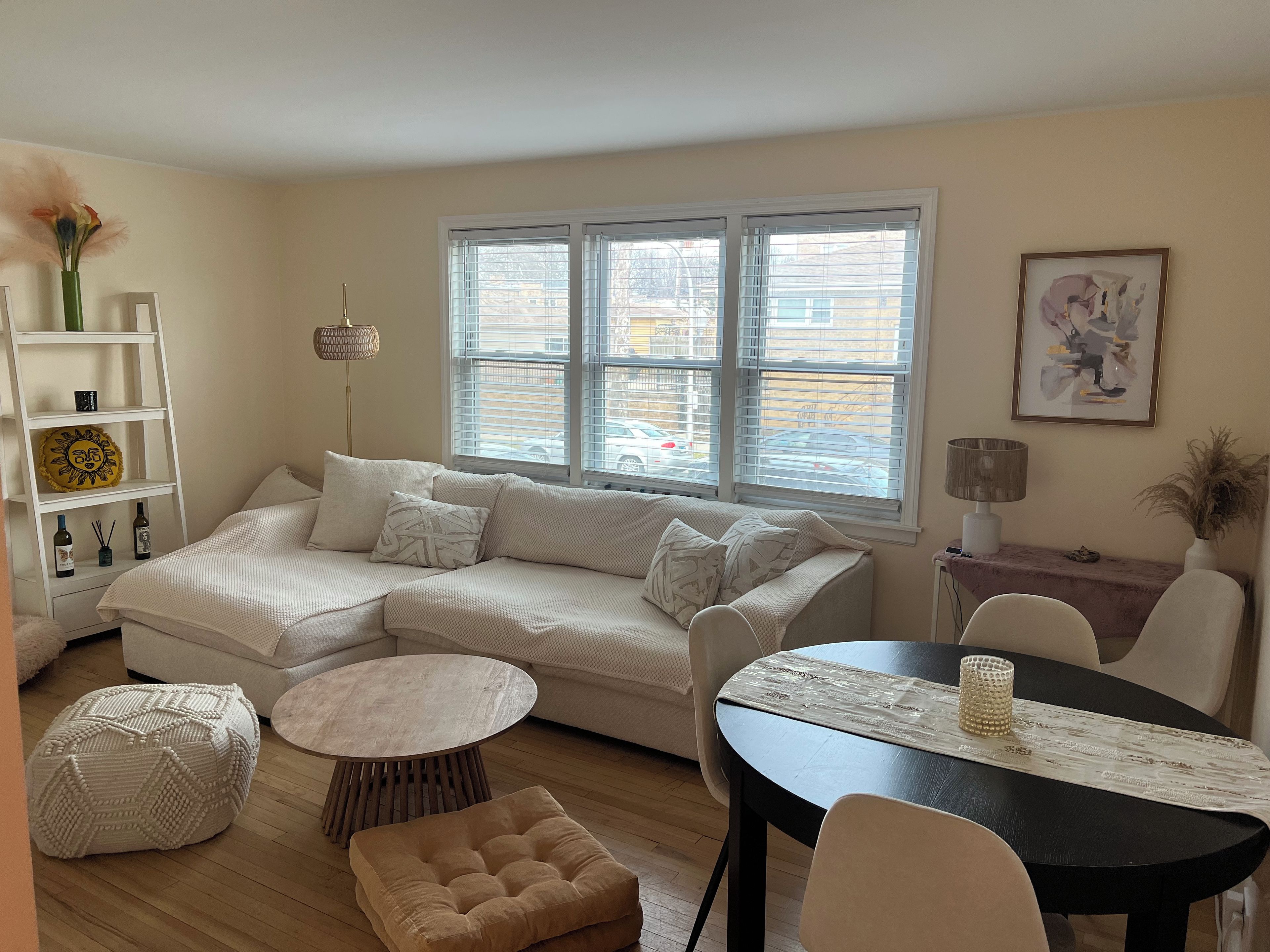 A living room with a sectional sofa, a round coffee table, a small ottoman, and a dining table with chairs.