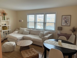 A living room with a sectional sofa, a round coffee table, a small ottoman, and a dining table with chairs. - Cozy 2-bedroom condo with AC in gorgeous Chicago neighborhood (Chicago)